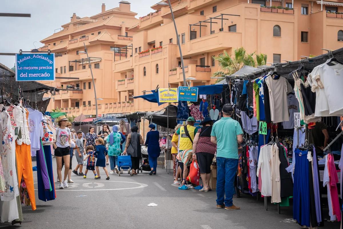 Mercadillo de Roquetas de Mar un jueves con varios puestos de ropa en la calle y múltiples personas caminando y observando los puestos en la vía.